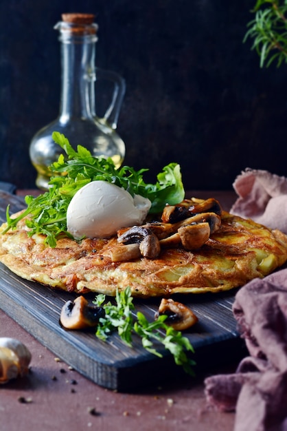 Frittata mit Kartoffeln, Pilzen, Rucola und Kräutern zum Frühstück auf dunklem Hintergrund.