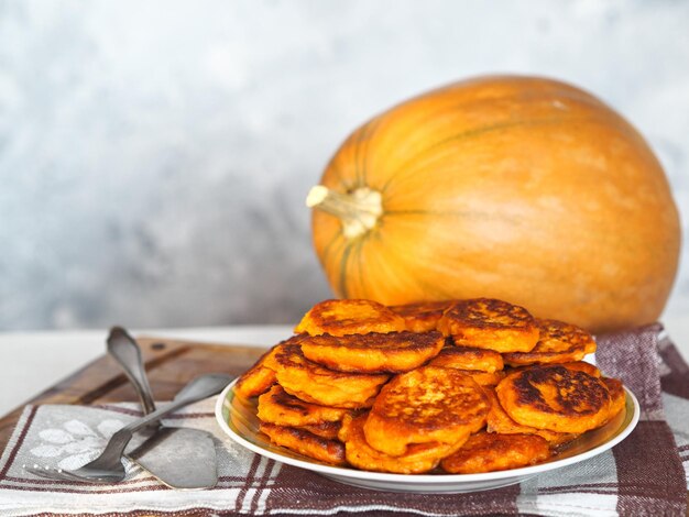 Frittierte Kürbis-Pancakes auf einem Teller auf dem Hintergrund eines großen orangefarbenen Kürbis