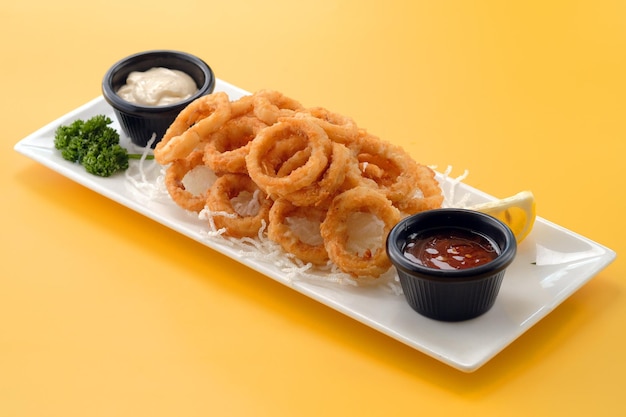 Frittierte Vorspeise Bangkok Calamari-Ringe mit Mayo-Dip und Tomatensauce, serviert in einem Gericht isoliert auf gelbem Hintergrund Seitenansicht von Fastfood