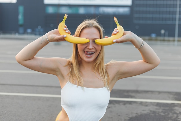 Frivole und schelmische junge Frau mit Zahnspange, die Bananen im Gesicht hält, hat Spaß...