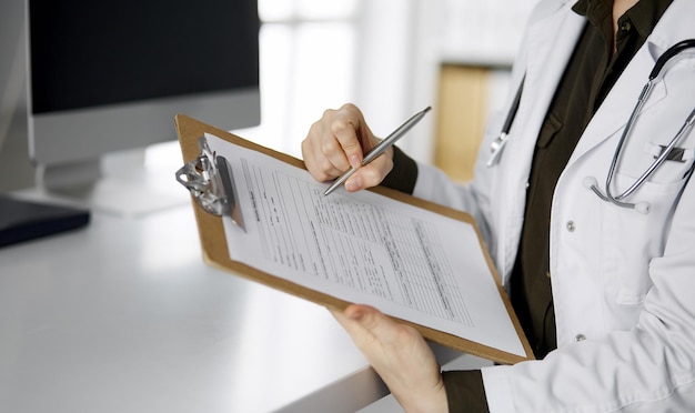 Fröhlich lächelnde Ärztin mit Klemmbrett in der Klinik. Porträt einer freundlichen Ärztin am Arbeitsplatz. Perfekte medizinische Versorgung im Krankenhaus. Medizin-Konzept.