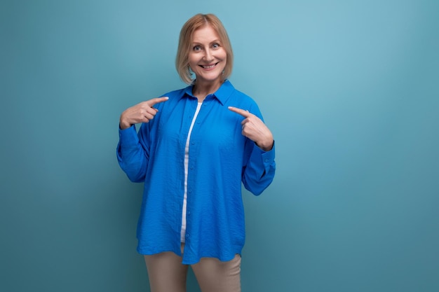 Fröhlich lächelnde Frau mittleren Alters in einem blauen Hemd auf blauem Hintergrund mit Kopierraum