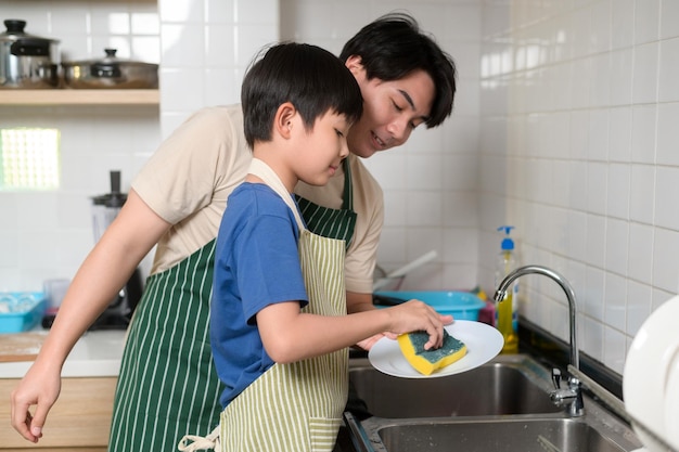 Fröhlich lächelnder junger asiatischer Vater und Sohn beim Abwasch in der Küche zu Hause