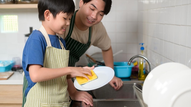 Fröhlich lächelnder junger asiatischer Vater und Sohn beim Abwasch in der Küche zu Hause