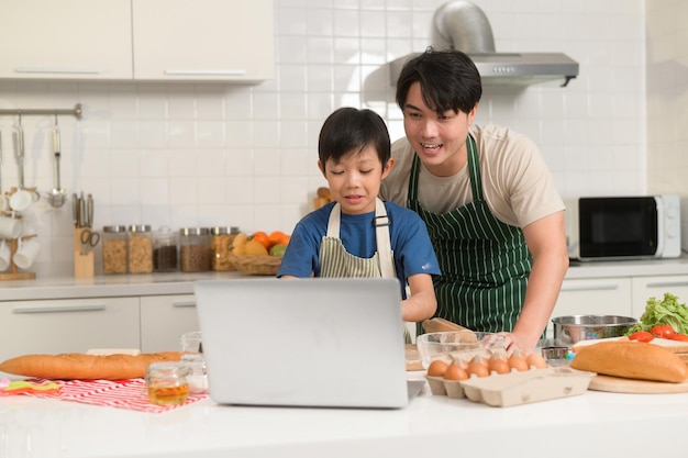 Fröhlich lächelnder junger asiatischer Vater und Sohn, die Mutter per Videoanruf anrufen, genießen das Kochen in der Küche