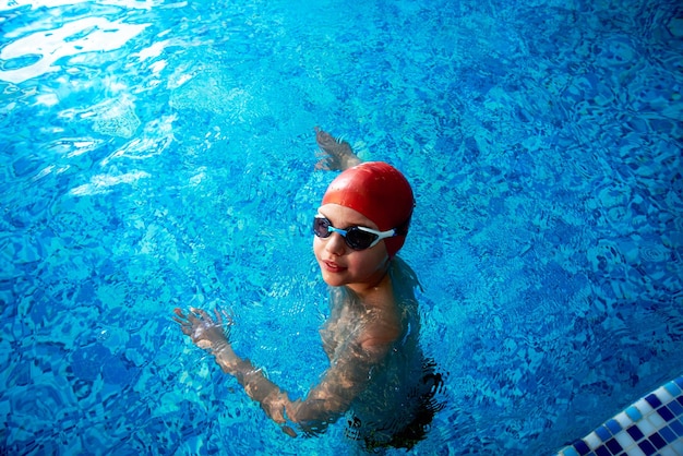 Fröhlich lächelnder Schwimmer mit Mütze und Brille lernt professionelles Schwimmen im Schwimmbad im Fitnessstudio aus nächster Nähe