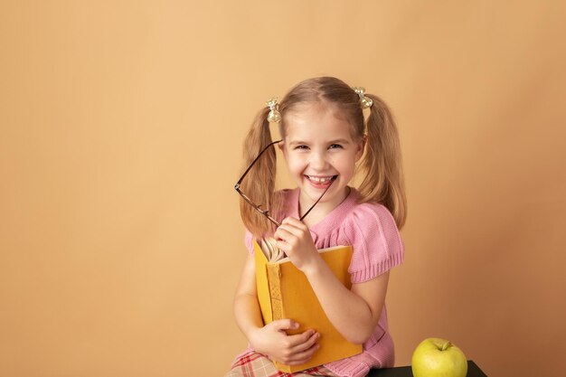 Fröhlich lächelndes kleines Mädchen mit Büchern und Rucksack lächelnd und mit Blick auf die Kamera Back to School