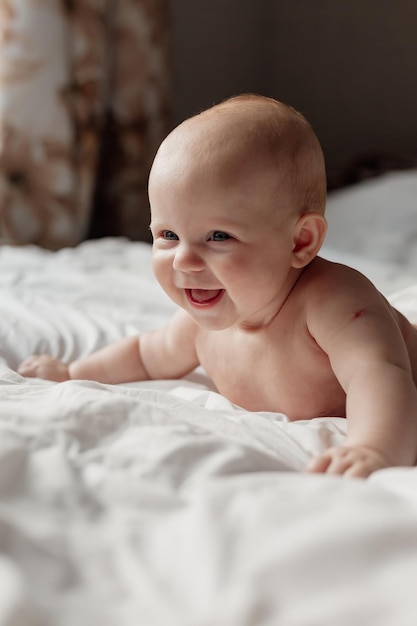 Fröhlich lächelndes neugeborenes Baby in einer Windel liegt auf seinem Bauch auf einem weißen Bett