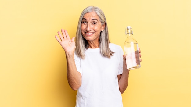 Fröhlich und fröhlich lächeln, mit der Hand winken, begrüßen und begrüßen oder sich verabschieden und eine Wasserflasche halten