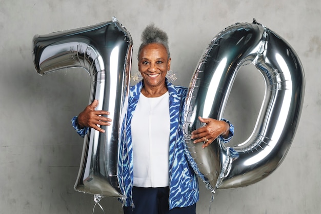 Fröhliche ältere Frau mit silbernen Ballons für ihre 70. Geburtstagsfeier