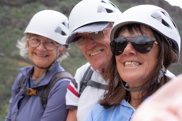 Fröhliche ältere Wanderfreunde mit Rucksäcken und Helmen, die den Trekkingtag auf dem Gipfel des Berges genießen