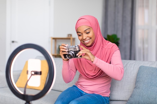 Fröhliche afrikanisch-amerikanische Bloggerin filmt Videokritik auf Retro-Kamera, während sie sitzt