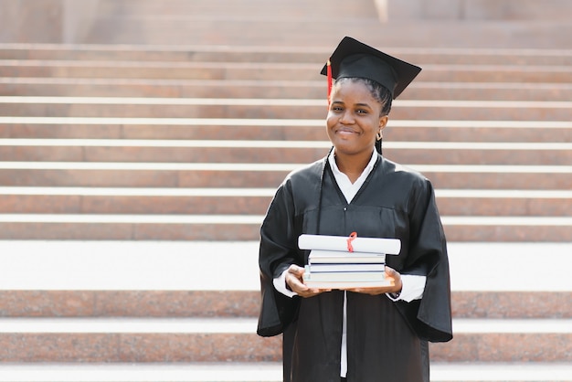 Fröhliche afroamerikanische Absolventin, die vor dem Universitätsgebäude steht