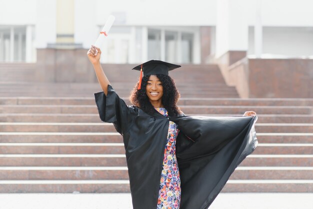 Fröhliche afroamerikanische Absolventin, die vor dem Universitätsgebäude steht