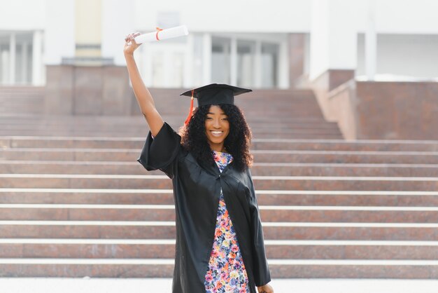 Fröhliche afroamerikanische Absolventin steht vor dem Universitätsgebäude