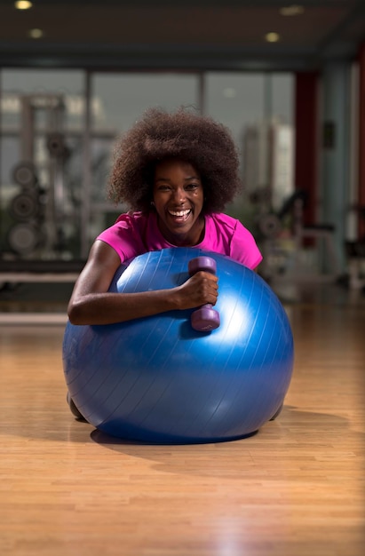 Fröhliche afroamerikanische Frau mit einer lockigen Afro-Frisur in einem Fitnessstudio, das sich nach dem Pilates-Training entspannt