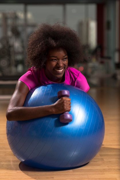 Fröhliche afroamerikanische Frau mit einer lockigen Afro-Frisur in einem Fitnessstudio, das sich nach dem Pilates-Training entspannt