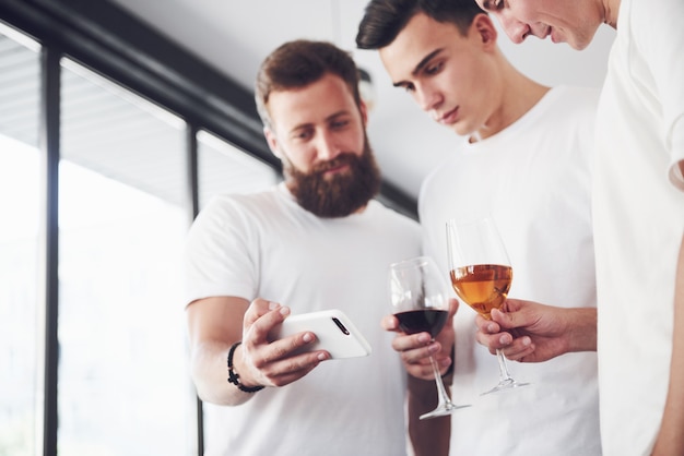 Fröhliche alte Freunde kommunizieren miteinander und telefonieren mit einem Glas Whisky oder Wein in der Kneipe. Konzept von Unterhaltung und Lifestyle. Wifi verband Leute in Stehtischbesprechung.
