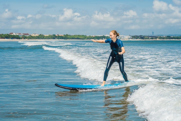 Fröhliche Anfänger-Surferin der jungen Frau mit blauer Brandung hat Spaß auf kleinen Meereswellen. Aktiver Familienlebensstil, Wassersportunterricht im Freien und Schwimmaktivitäten in den Sommerferien des Surfcamps.