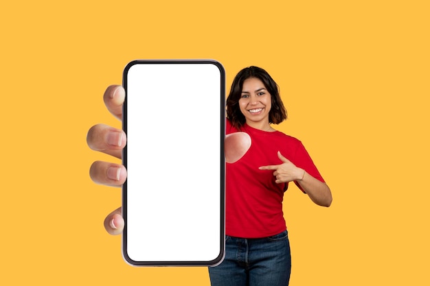 Fröhliche arabische Frau, die auf ein Handy mit leerem Bildschirm zeigt