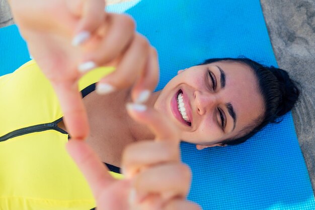 Fröhliche asiatische brünette Frau in stylischen gelben Leggings und Fitness-BH-Trainingskörper am Strand am Morgen Goa