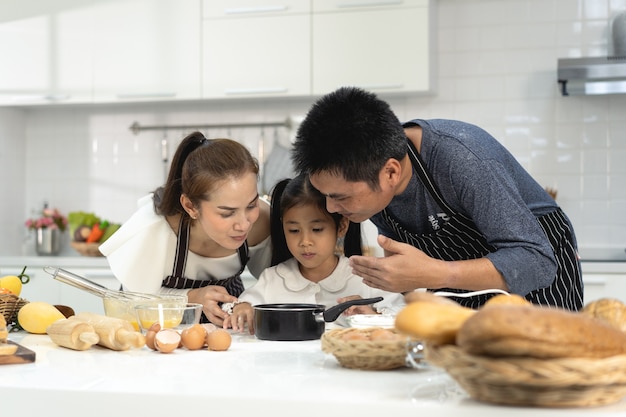 Fröhliche asiatische Familie mit Tochter, die Teig beim Backen von Keksen herstellt, Tochter hilft den Eltern bei der Vorbereitung des Backen-Familienkonzepts