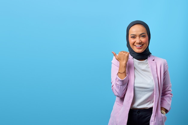 Fröhliche asiatische Frau, die mit dem Finger auf den leeren Raum über blauem Hintergrund zeigt