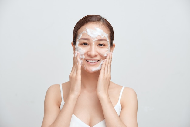Fröhliche asiatische Frau, die schäumendes Reinigungsmittel anwendet, hat saubere frische gesunde Haut.