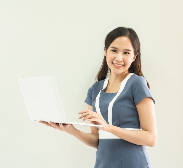 Fröhliche asiatische Frau im schönen Anzug, der Hand hält Laptop lokalisiert über graue Wand.