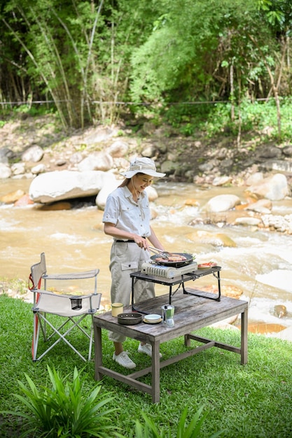 Fröhliche asiatische Frauen, die eine Barbecue-Lunchparty vorbereiten und einige Steaks mit dem Picknickofen grillen