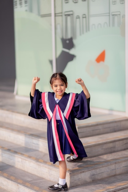 Fröhliche asiatische Mädchen in Abschlusskleidern an ihrem Abschlusstag in der SchuleAbschlusskonzept mit Kopierraumx9