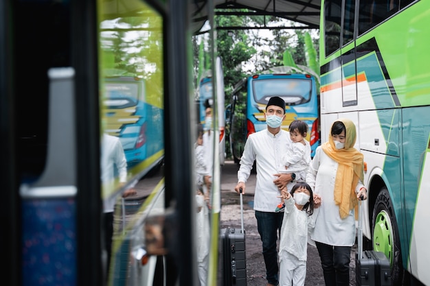 Fröhliche asiatische muslimische Urlaubsreise, die zusammen mit der Familie einen Bus fährt und eine Maske trägt, die die Ausbreitung des Virus verhindert