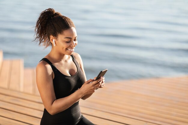 Fröhliche athletische schwarze Frau mit Smartphone beim Training