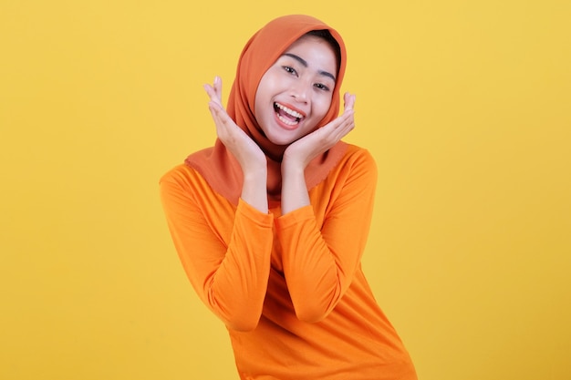 Fröhliche attraktive asiatische frau demonstriert kopierraum auf leerer gelber wand, hat einen fröhlichen freundlichen ausdruck, lässig gekleidet mit hijab, posiert drinnen