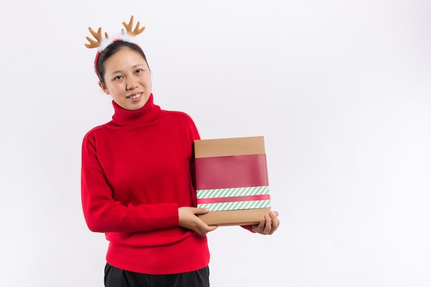 Fröhliche attraktive Frau im roten Kleid, die Spaß hat, während sie auf der großen Geschenkbox sitzt, die auf einem weißen Hintergrund isoliert ist