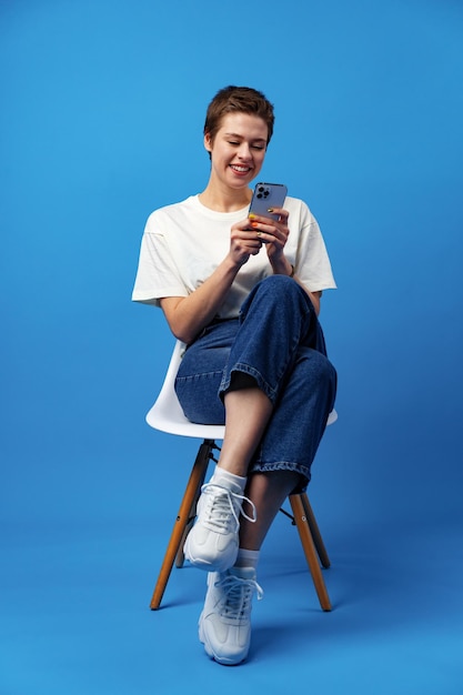 Fröhliche attraktive junge Frau mit Smartphone genießt das Chatten oder Online-Shopping vor blauem Hintergrund