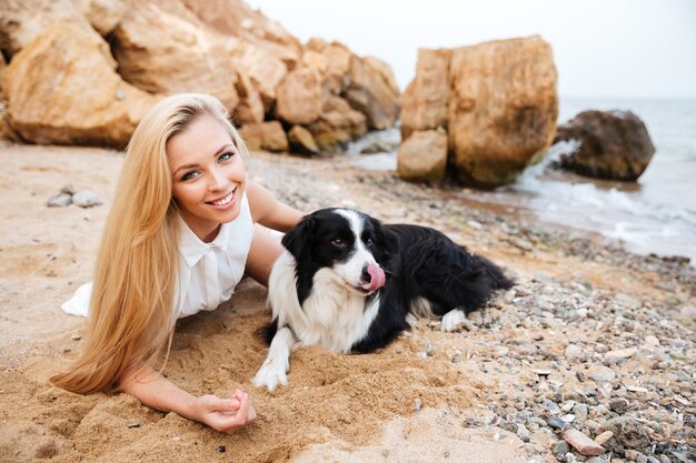 Fröhliche attraktive junge Frau ruht mit Hund am Strand