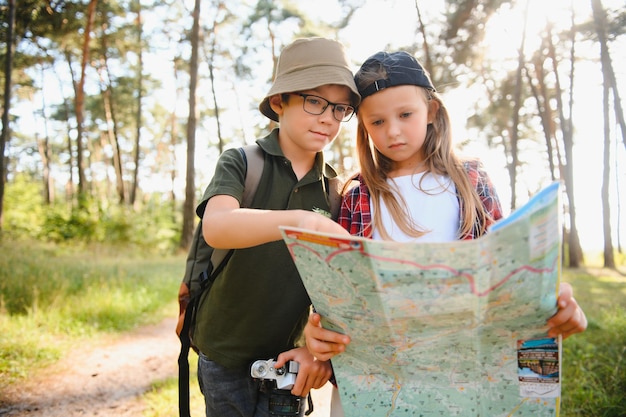 Fröhliche, aufgeregte Schulkinder mit Rucksäcken in Freizeitkleidung, die an einem sonnigen Herbsttag im Wald spazieren gehen. Zwei aktive Kinder, Junge und Mädchen, laufen und spielen zusammen während eines Campingausflugs in der Natur