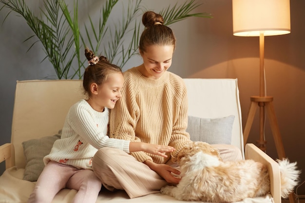 Fröhliche, begeisterte Familie, die Zeit zu Hause verbringt und auf dem Sofa sitzt und mit der Freizeit des Hundes spielt