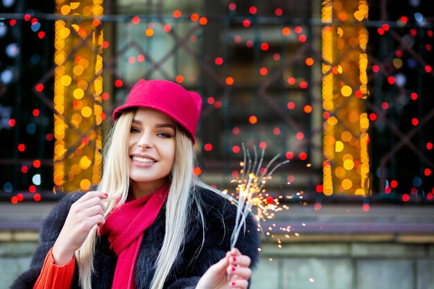 Fröhliche blonde Frau, die Neujahr mit Wunderkerzen an den verschwommenen Lichtern der Stadt feiert. Platz für Text