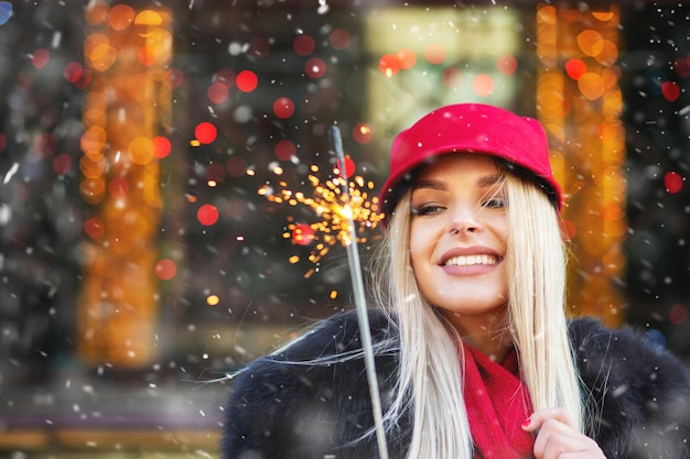 Fröhliche blonde Frau, die Spaß mit funkelnden Lichtern auf dem Weihnachtsmarkt hat. Platz für Text