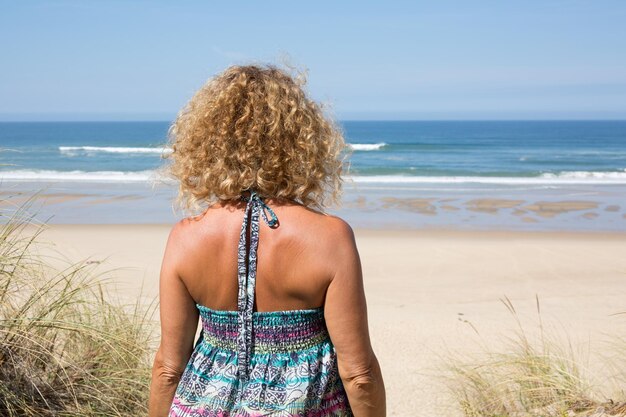 Fröhliche Blondine, die im Meer steht und an einem sonnigen Tag posiert