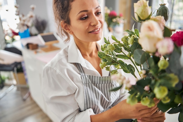 Fröhliche brünette Dame, die eine Blumenkomposition bewundert