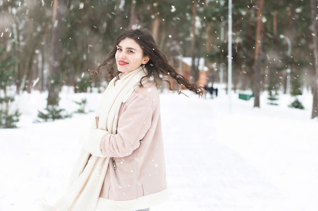 Fröhliche Brunettefrau, die während des Schneefalls in den Wald geht. Platz für Text