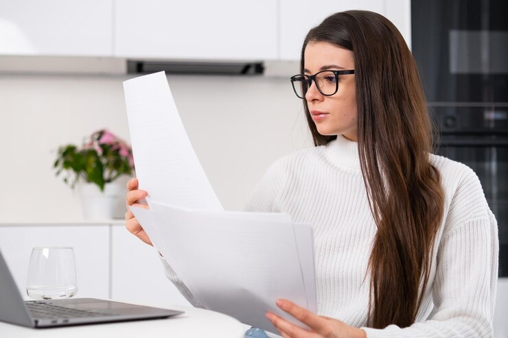 Fröhliche Dame, die Papier in der Hand hält, nutzt einen Computer und arbeitet aus der Ferne