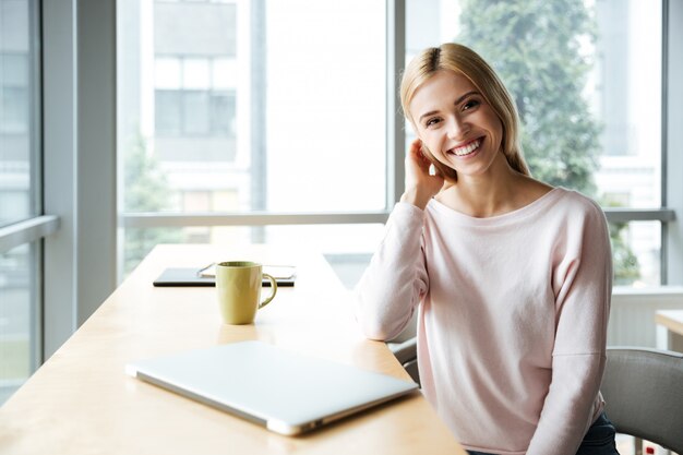 Fröhliche Dame im Büro Coworking sitzen in der Nähe von Laptop-Computer