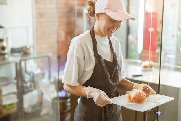 Fröhliche Dame in Schürze trägt ein Tablett in einer schön dekorierten Bunsin-Handwerksbäckerei