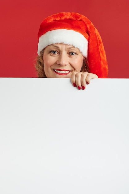 Fröhliche Dame in Weihnachtsmütze mit einem weißen Brett, Kopienraum für Ihre Werbung.