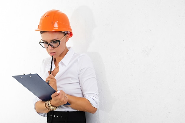 Fröhliche Dame mit kurzen dunklen Haaren, im schönen Büroanzug, orange Bauhelm plant etwas mit Tablette auf Weiß isoliert