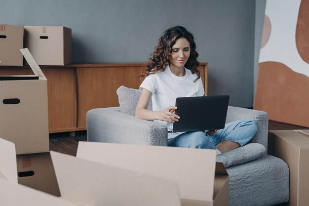 Fröhliche Dame sitzt im Sessel und arbeitet mit dem PC Lieferservice über das Internet bestellen